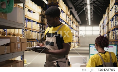 Woman employee placing adhesive shipping labels on boxes in depot, labeling packages with awb tracking numbers to ensure seamless express delivery and order processing. Camera A. 130428703