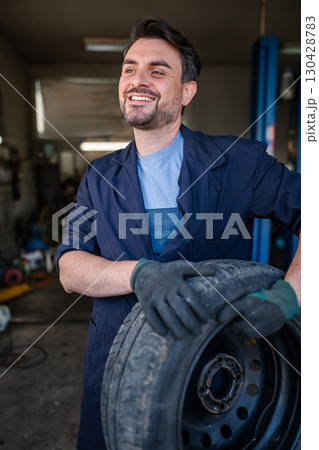 Mechanic holding a tire and smiling in a garage 130428783