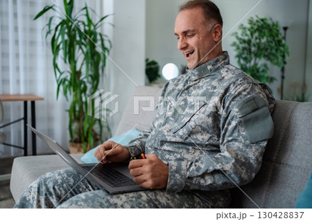 Happy soldier buying online with credit card and laptop 130428837