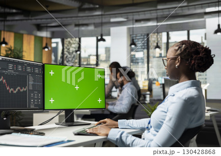 Trader in prop firm office using using trading app on green screen mockup PC to analyze market data and execute trades. Woman monitoring stock exchange using chroma key isolated screen computer 130428868