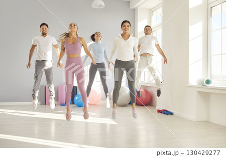 Group of happy sporty men and women doing jumping exercise during fitness workout at gym Group of happy sporty men and women doing jumping exercise during fitness workout at gym 130429277