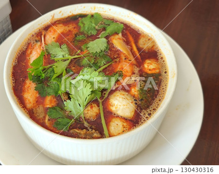 Hot and steamy bowl of tom yum soup with shrimp, mushrooms, and herbs in a spicy red broth, served fresh in a white ceramic bowl. 130430316