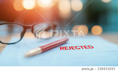 Rejected document with red stamp, pen, and glasses on table, evoking disappointment and reflection on missed opportunities 130431033