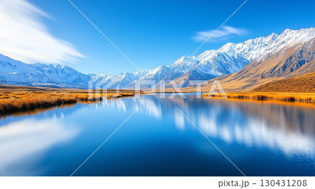 Landscape background serene alpine valley with tranquil lake reflecting snow capped mountains under clear blue sky. golden grass adds warmth to stunning landscape 130431208