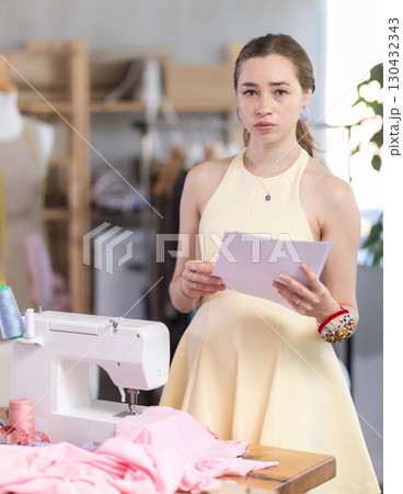 Upset young woman seamstress with documents in workshop 130432343