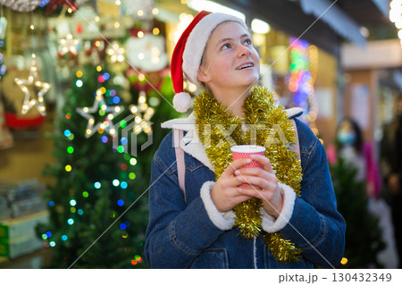 Teenagers girl holding hot cup of coffee in hands at street christmas fair Teenagers girl holding hot cup of coffee in hands at street christmas fair 130432349