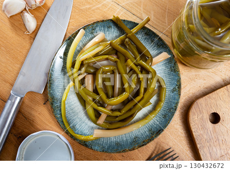 Pickled ramson is laid out on plate, next to it is cutting board, garlic cloves, knife and cutting board Pickled ramson is laid out on plate, next to it is cutting board, garlic cloves, knife and cutting board 130432672