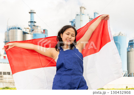 Happy asian girl in work clothes with flag of indonesia standing in front of industrial scenery 130432908