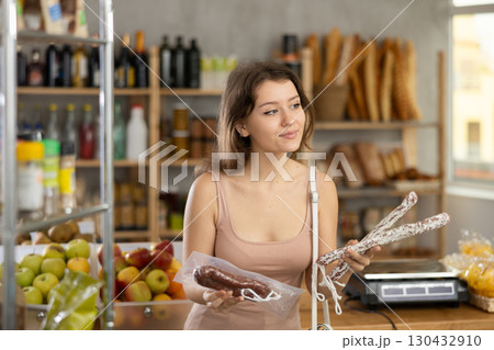 Young girl choosing dried sausages in grocery store 130432910