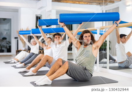 Men and women practicing pilates with roller on gray mat in gym room 130432944