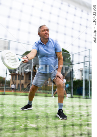 View through tennis net of elderly man playing paddle tennis 130432959