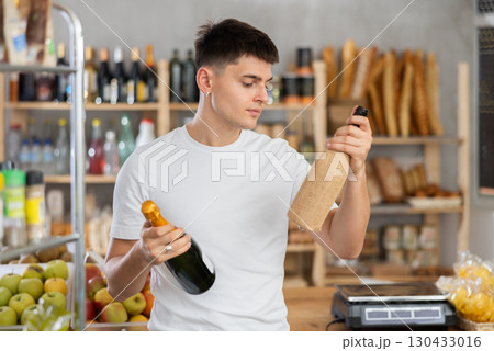 Guy carefully chooses spark wine or traditional wine in grocery store Guy carefully chooses spark wine or traditional wine in grocery store 130433016