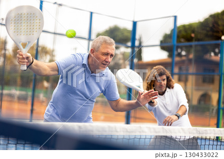 Aged man playing paddleball match on outdoor court 130433022