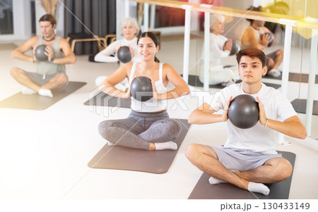 Group of cheerful sports people of different ages practicing pilates with a ball in the gym of a modern fitness studio. 130433149
