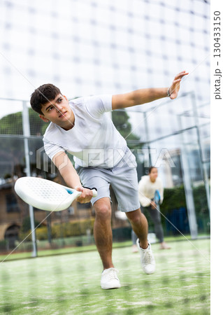 Sportive young man playing padel together with a partner. View through tennis net 130433150