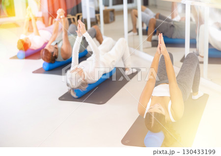Men and women practicing pilates with roller on gray mat in gym room Men and women practicing pilates with roller on gray mat in gym room 130433199