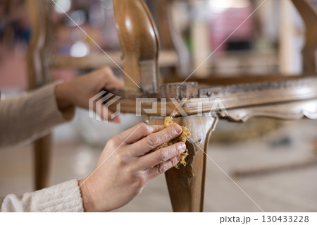 Close up of artisan hand applying wax to old vintage chair in furniture workshop 130433228