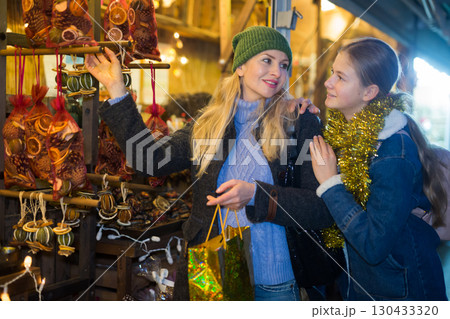 Smiling teen girl with mother choosing Christmas decorations at street fair Smiling teen girl with mother choosing Christmas decorations at street fair 130433320