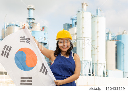 Portrait of teenage girl in blue overalls with flag of South Korea in her hands against the backdrop of modern metallurgical plant 130433329
