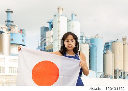 Sad young woman with flag of Japan against background of factory 130433332