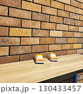 Two small, orange toy cars rest on a light wooden surface near the brick wall  130433457