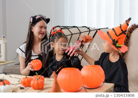 Three smiling kids in costume celebrate halloween day, two with jack o lanterns and one with bloody hand decorations enjoy the festive occasion at home. 130433906