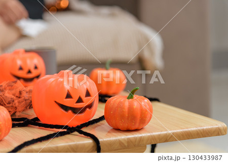 Festive orange pumpkins sit on a wood table, some feature carved faces and black pipe cleaner accents are added to complete a seasonal decoration displayed indoors. 130433987