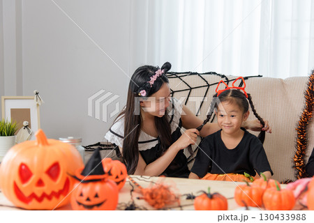 A woman in a cat ear headband styles hair for children with fox ears, a Halloween theme shows with pumpkins, a mini broom, spiders and cute ghost decors. 130433988