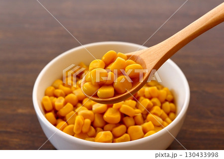 テーブル背景の木製スプーンですくったとうもろこしの粒 130433998