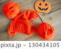 Orange wool and knitting needles with decorative pumpkin. Halloween still life. Cozy lifestyle concept. Autumn lifestyle. October background. Bright needlework and smiling pumpkin. Knitted fashion 130434105