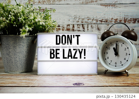Don't Be Lazy! text on light box with alarm clock on wooden background 130435124