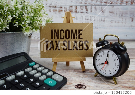 Income Tax Slabs text with alarm clock and calculator on wooden background 130435206