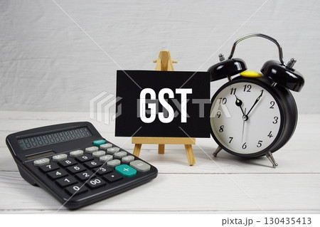 GST  abbreviation of Goods and Service Tax text with alarm clock on wooden background 130435413