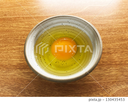 Fresh raw egg with golden yolk and clear egg white in ceramic bowl on wooden table, minimal style food photography highlighting natural texture, cooking ingredient and healthy protein source 130435453