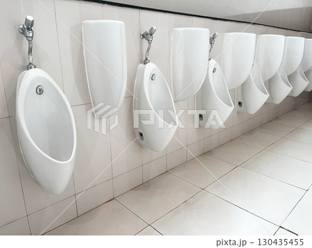 Row of white ceramic urinals in a public restroom, clean and organized sanitary facility with tiled walls and floor, representing hygiene, infrastructure, and modern bathroom interior design 130435455