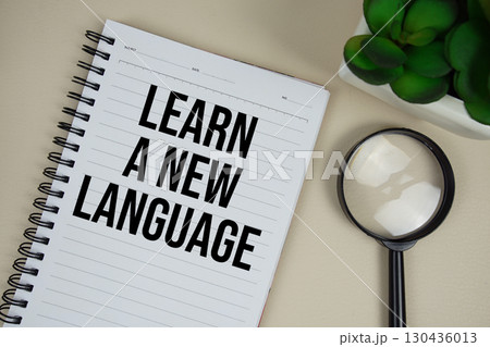 Learn A New Language text on paper notebook with magnifying glass on beige leather background 130436013