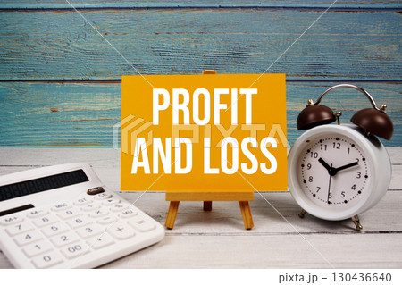 Profit And Loss text written on paper card with calculator and alarm clock on wooden background 130436640