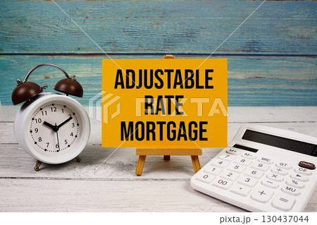Adjustable-Rate Mortgage (ARM) text written on paper card with calculator and alarm clock on wooden background 130437044