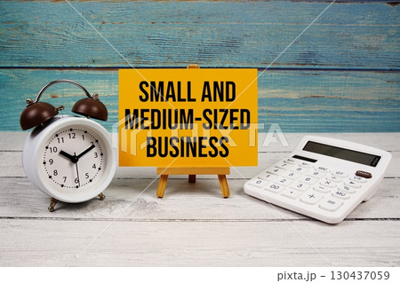 SMB Small and Medium-Sized Business text written on paper card with calculator and alarm clock on wooden background 130437059