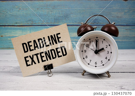 Deadline Extended text written on paper card with alarm clock on wooden background Deadline Extended text written on paper card with alarm clock on wooden background 130437070