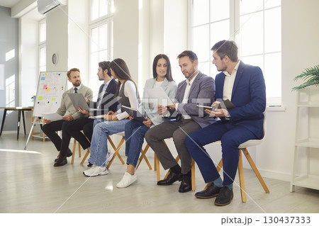 Team of office workers sitting in row on comfortable chairs and discussing something Team of office workers sitting in row on comfortable chairs and discussing something 130437333