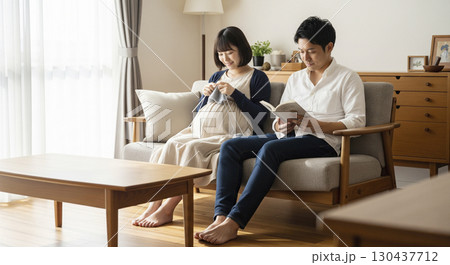 妊婦中の妻が編み物をし、夫がそばで本を読む光景 130437712