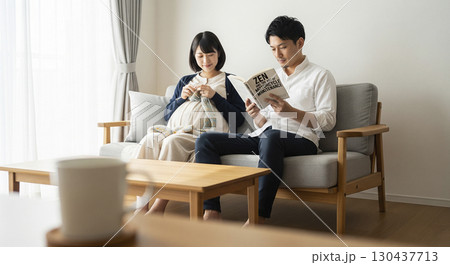 妊婦中の妻が編み物をし、夫がそばで本を読む光景 130437713