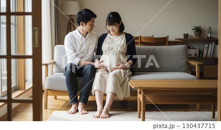 ソファでお腹をさする妊娠中の妻を優しく見守る夫 130437715