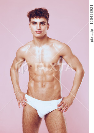 Confident young man with athletic build posing in white swimwear against a pastel pink background. Fitness and body positivity concept. Confident young man with athletic build posing in white swimwear against a pastel pink background. Fitness and body positivity concept. 130438921