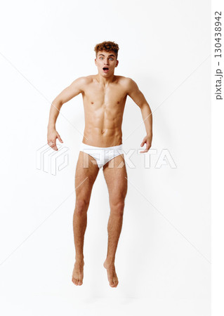 Surprised young man jumping with excitement, showcasing toned physique. White background emphasizing his expression and movement. Fitness and emotion concept. 130438942