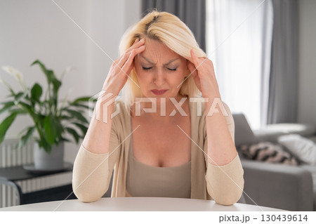 Blonde middle aged woman sitting at home office desk, head down, covering eyes with one hand, crying silently, reflecting loneliness and inner struggle Blonde middle aged woman sitting at home office desk, head down, covering eyes with one hand, crying silently, reflecting loneliness and inner struggle 130439614
