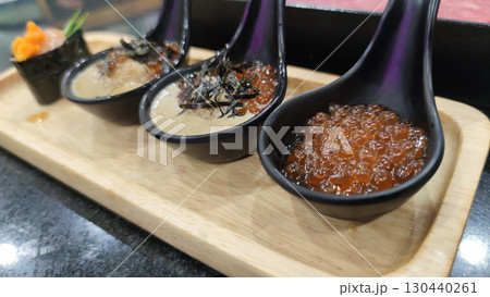 Salmon roe and creamy sauce served in black spoons on wooden tray, showcasing fresh and vibrant seafood appetizer with delicate texture and rich flavor 130440261