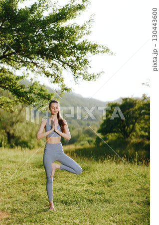 Young woman practicing yoga in nature, wearing gray activewear, embodying tranquility and mindfulness amidst green landscapes Young woman practicing yoga in nature, wearing gray activewear, embodying tranquility and mindfulness amidst green landscapes 130443600