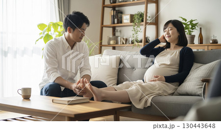 ソファに横たわる妊婦の足をマッサージする夫 130443648